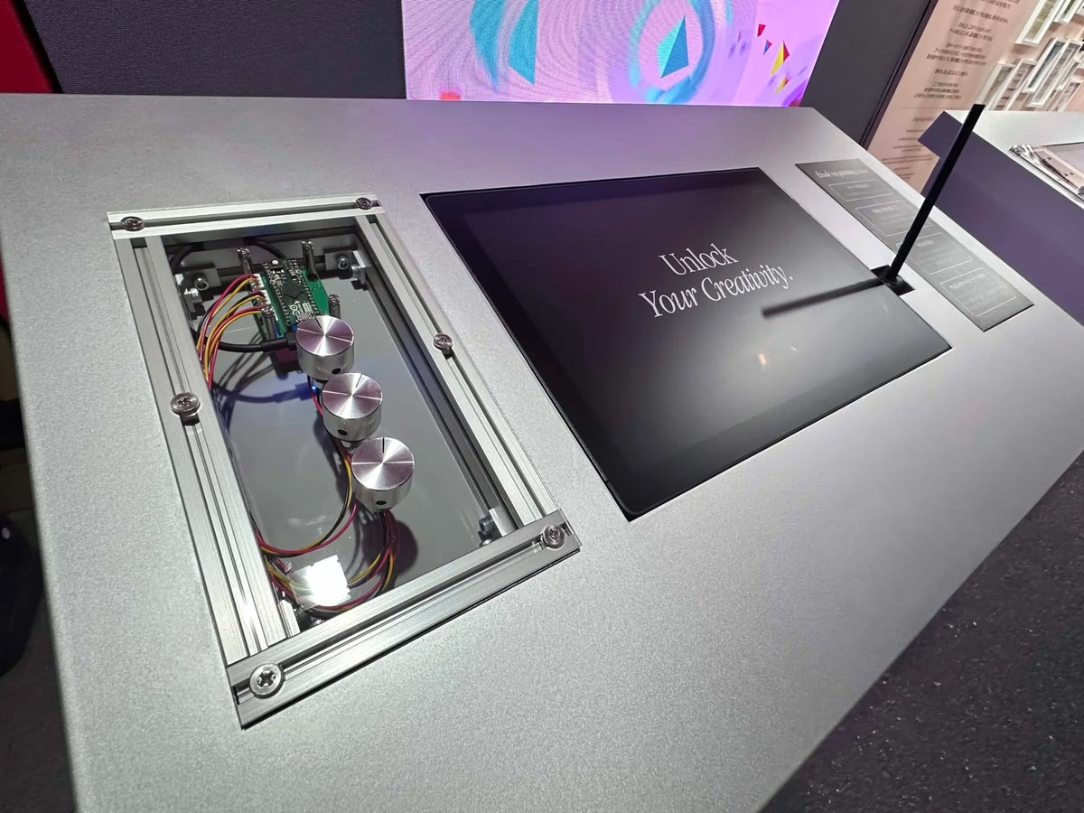 The installation's physical interface: a console with three metal dials, a pen tablet, and the exposed microcontroller that reads them.