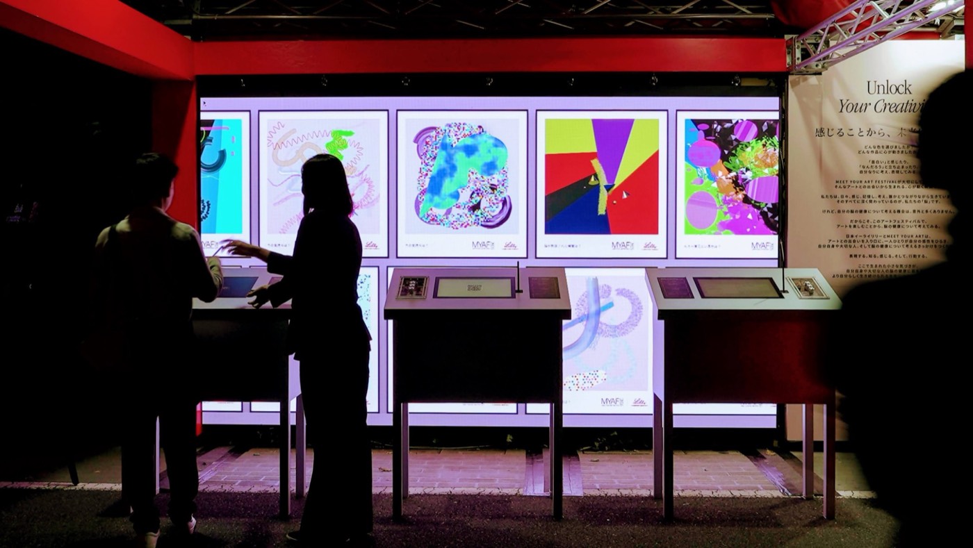 Visitors drawing at the Unlock installation, with a wall of finished works behind them.